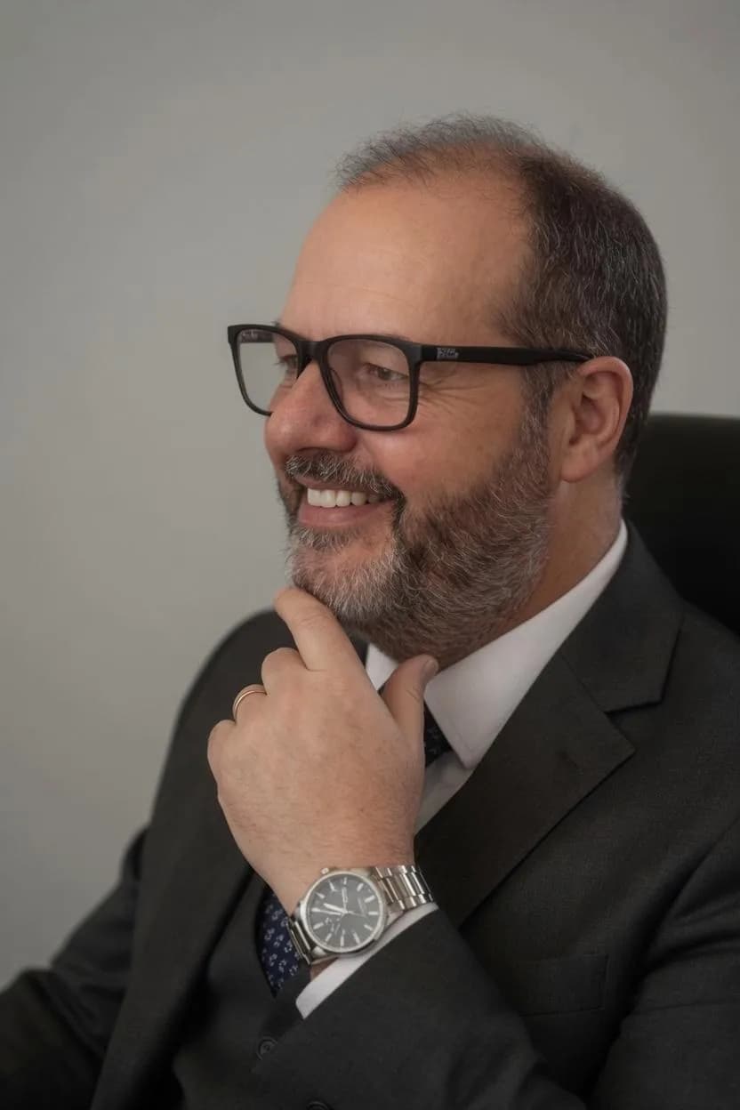 Advogado de óculos e terno escuro, sentado, com a mão no queixo e sorrindo
